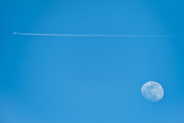 A nice picture of the moon at five in the afternoon with a passenger plane leaving a trail in the...
