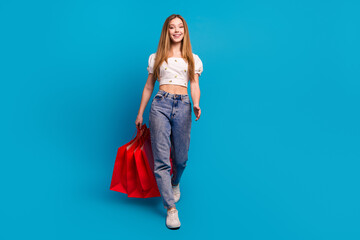 Full size photo of nice young girl walk hold bags empty space wear top isolated on blue color background