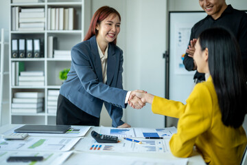 Fototapeta premium A woman shakes hands with another woman in a yellow jacket. The two women are in a business setting, with a white board behind them