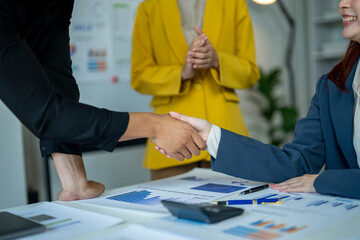 Three women shake hands in a business meeting. The woman on the left shakes hands with the woman in...