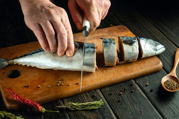 Cooking fish on a kitchen board. A knife in the hand of a cook for slicing mackerel before salting.