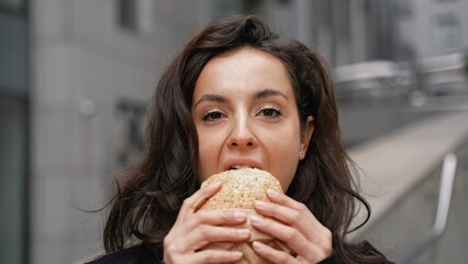 Close up. Young beautiful caucasian woman eating very tasty burger, looking into the camera, and...