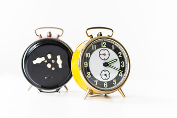 Retro vintage yellow alarm clock with a white dial, set against a white background. In the background, there is an identical clock facing backward, showcasing its white knobs against a black casing.