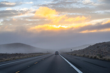 road in the mountains with raining and misty above the mountain contrast with red clouds shining by the sunset behind background, unrecognized car in the middle, Big Island Hawaii USA