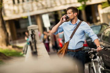 Smiling businessman with bicycle holding coffee cup in urban setting