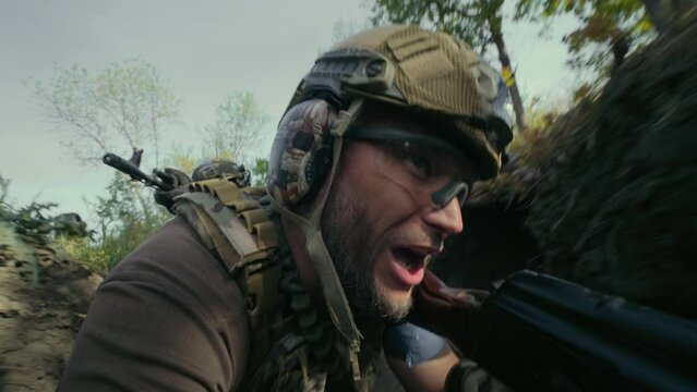 Close up portrait of Ukrainian soldier or commander in camouflage and helmet running through trench with rifle gun, talking to colleague during assault on enemy positions. War or military conflict.