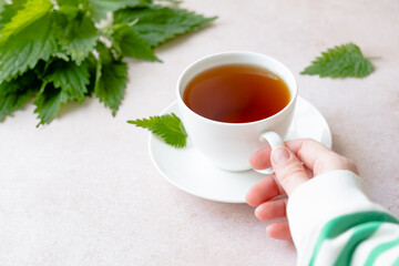 Herbal nettle tea with fresh nettle leaves. White cup of nettle tea on a table. Weight loss and...