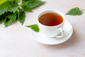 Herbal nettle tea with fresh nettle leaves in a white cup on a table. Weight loss and detox....
