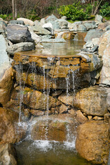 An artificial waterfall with flowing water and stone structures. Authentic landscape overlooking a spring garden.	