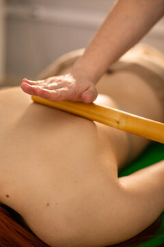 Closeup of a masseur's hands making a bamboo stick massage to a redhead woman client during spa procedure