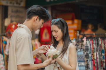 this adorable couple is eating and walking around at street food with happiness, they are dating on weekend at market, smiling because both of them are super satisfy being a couple