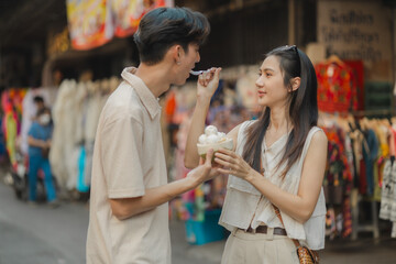 this adorable couple is eating and walking around at street food with happiness, they are dating on weekend at market, smiling because both of them are super satisfy being a couple
