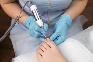 Pedicure expert performs a hardware pedicure on a woman, employing a nail drill