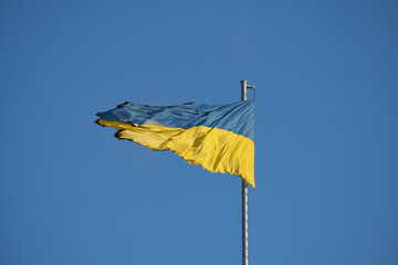 Burnt Ukrainian flag stands against the backdrop of a serene blue sky: Spirit of resilience. Symbol...