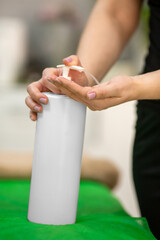 Closeup of a masseur pouring oil to her hand in a bright massage spa room