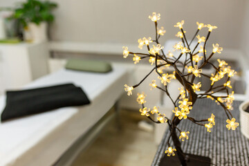 Bright modern massage room interior details, blurred massage couch table and sharp LED lamp in form of tree with leaves like flowers