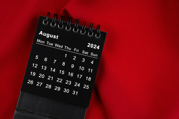 August 2024 Black spiral desktop calendar on red fabric.