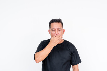A middle aged Asian man stands against a white background, blowing into his hand to check for bad...