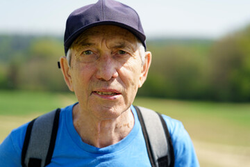 Portrait of senior man with backpack and cap looking at camera in countryside