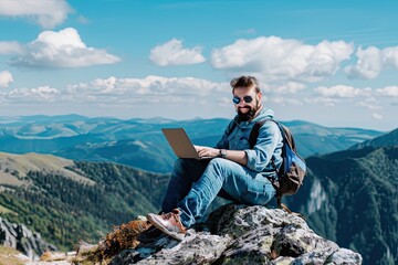 A digital nomad smiling while working on his laptop, seated on a mountain peak with a breathtaking view of the landscape around.