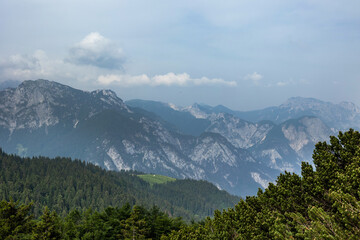 guardando verso l'orizzonte, leggermente dall'alto, ad un ambiente naturale di montagna, nel nord est Italia, avvolto da una leggera foschia e da delle nuvole, di giorno, in estate