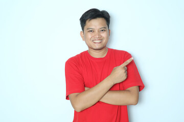 Young Asian man pointing finger to the left with smiling face. Wearing red t-shirt