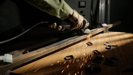 Craftsman in protective gloves and overall working with grinder at industrial plant, man silhouette grinding iron detail on the table in workshop.