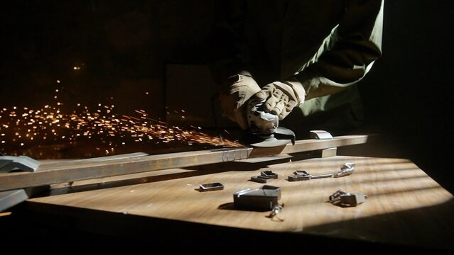 Craftsman in protective gloves and overall working with grinder at industrial plant, man silhouette grinding iron detail on the table in workshop. - Powered by Adobe