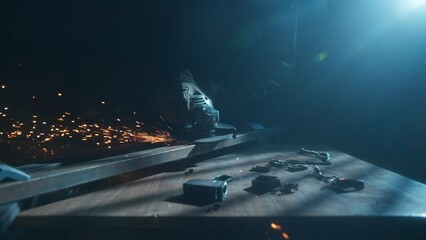 Craftsman in protective gloves and overall working with grinder at industrial plant, man silhouette grinding iron detail on the table in workshop.
