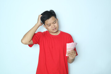 Asian man showing holding paper money and showing confused face expression. Wearing red t-shirt