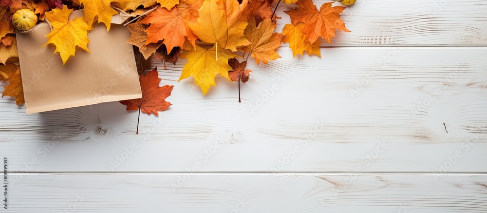 Poster Autumn themed arrangement featuring a paper bag filled with dried yellow leaves against a white wooden surface Captured from a top down perspective this flat lay image offers ample whitespace for cre