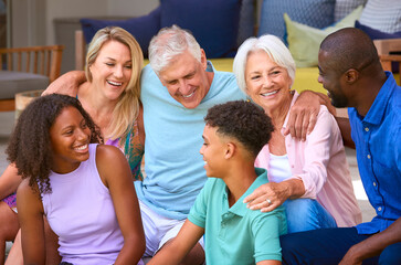 Three Generation Family Laughing And Smiling Sitting Outdoors At Home On Deck Together