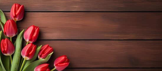 A top down view of red tulips displayed on a rustic wooden table with ample empty space for other elements in the image