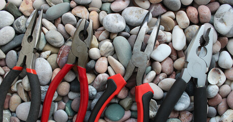 Top parts of variety types of pliers lined up in size comparison on a round smooth rocks concept...