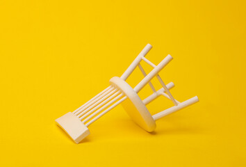 Inverted miniature chair on yellow background. Business concept