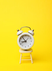 White mirniature chair with alarm clock on a yellow background. Business concept