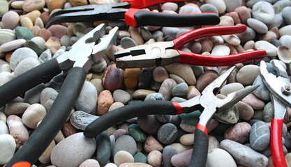 Variety types of pliers with rubberized handles laid out on a sea stones angle view
