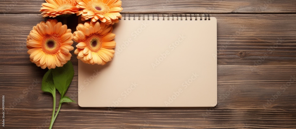 Aufkleber top view copy space image of three gerbera flowers and a blank paged notebook resting on a wooden ta