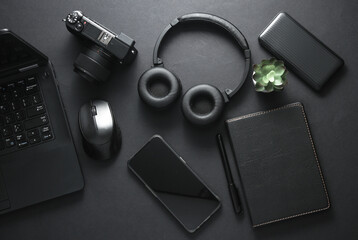 Modern black gadgets and accessories. Laptop, camera, smartphone, stereo headphones, notepad on a black background. Working space. Flat lay. Top view