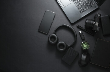 Modern gadgets and accessories in black. Laptop, camera, smartphone, stereo headphones, notepad, external hard drive, USB flash drive on a black background. Working space. Flat lay. Top view