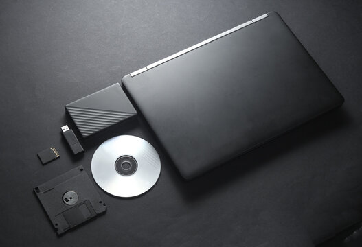 Outdated and modern digital storage media with laptop on black background