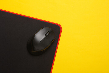 Black PC mouse with PC mouse pad on a yellow background