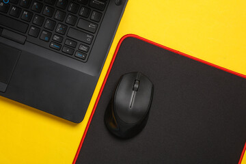 Black Laptop and PC mouse with PC mouse pad on a yellow background