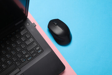 Black Laptop and wireless PC mouse on pink blue background. Top view