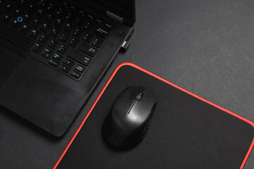 Black Laptop and PC mouse with PC mouse pad on a black background. Top view