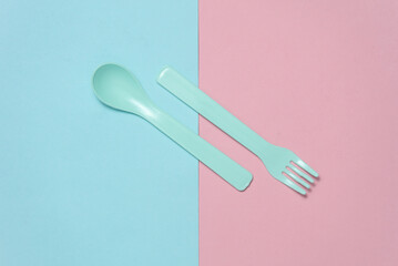 Plastic fork and spoon for baby on a blue pink background. Top view