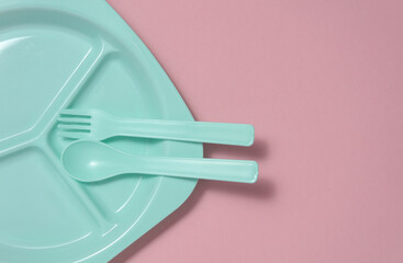 Separate plastic plate with spoon and fork for feeding baby on pink background. Top view