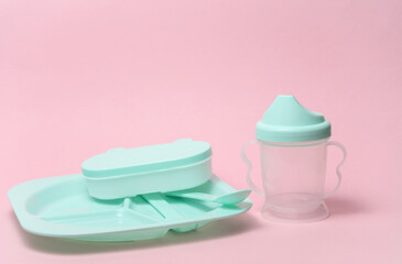 Plastic dishes for feeding a baby on a pink background