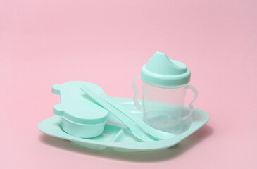 Plastic dishes for feeding a baby on a pink background