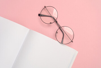 Open empty white notebook with eyeglass on a pink background. Template for design